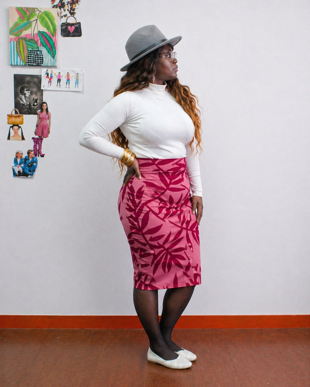 Person wearing a white long-sleeve top and pink leaf-patterned skirt with a gray hat indoors.